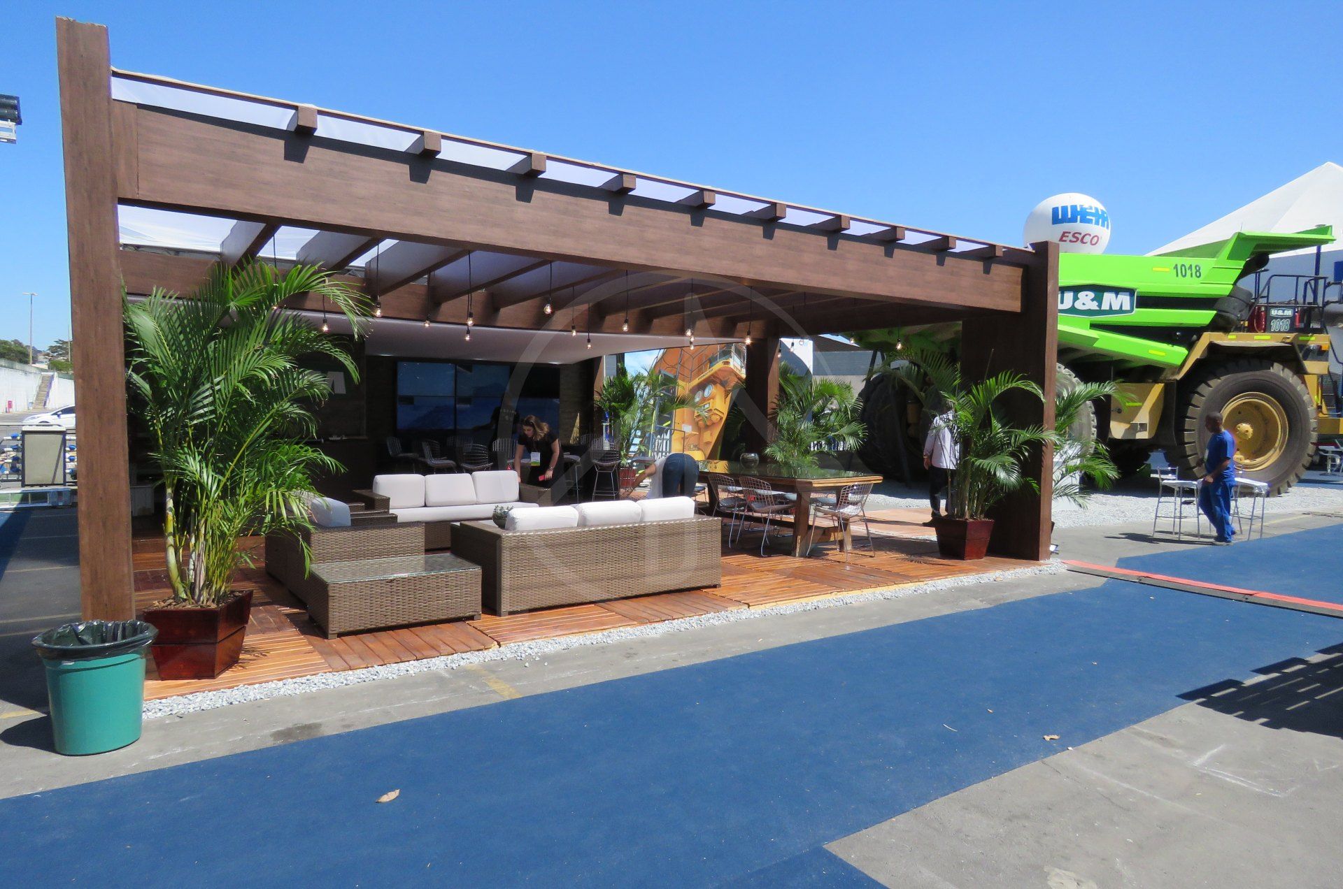 Estande construído com pergolado de madeira e jardim tropical em feira agropecuária, com um caminhão fora de estrada em exposição ao lado