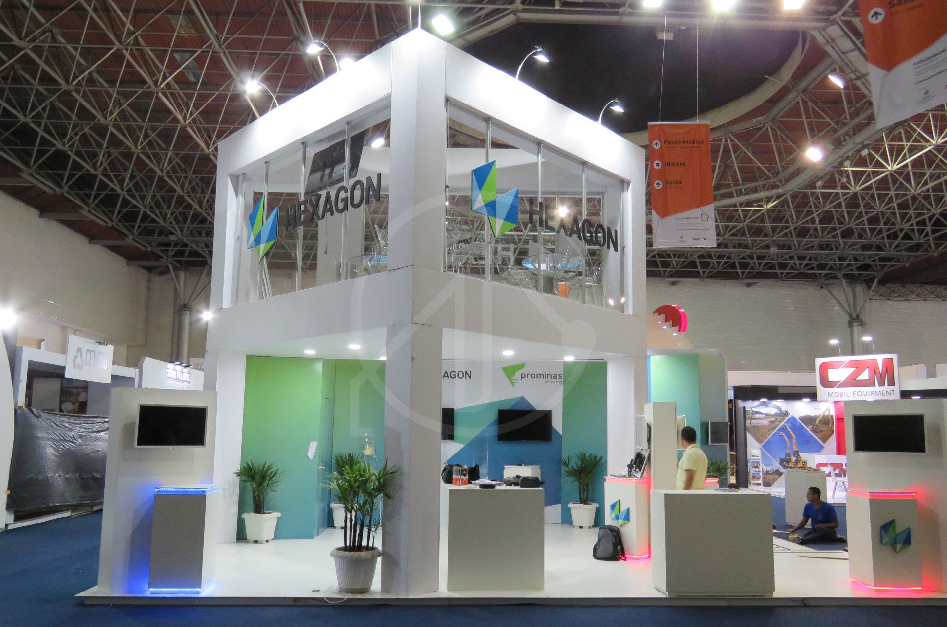 Estande de dois pavimentos com fachada branca e azul em pavilhão de feira