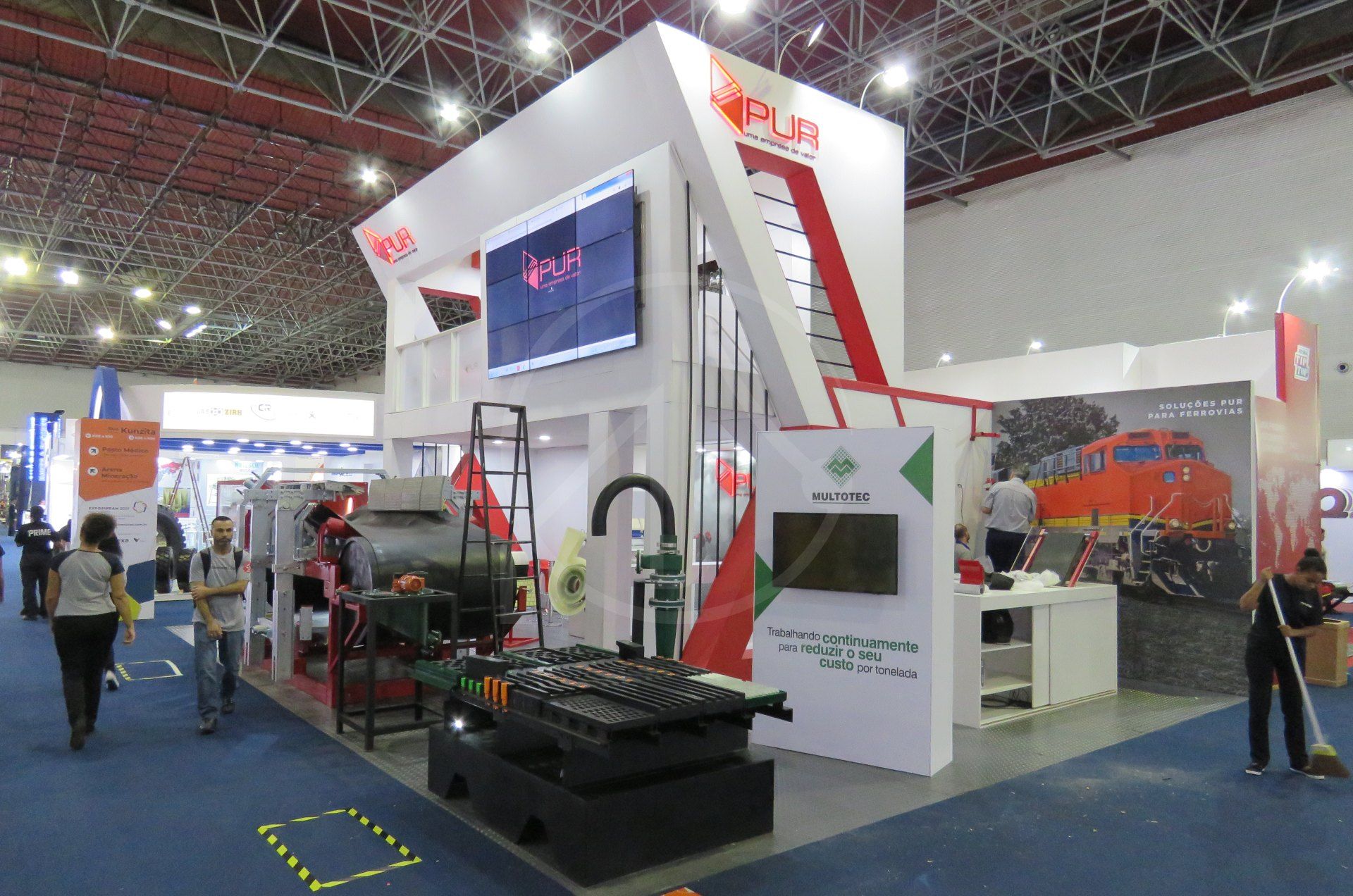 Estande construído branco de dois níveis com telão, dentro de um pavilhão de feira