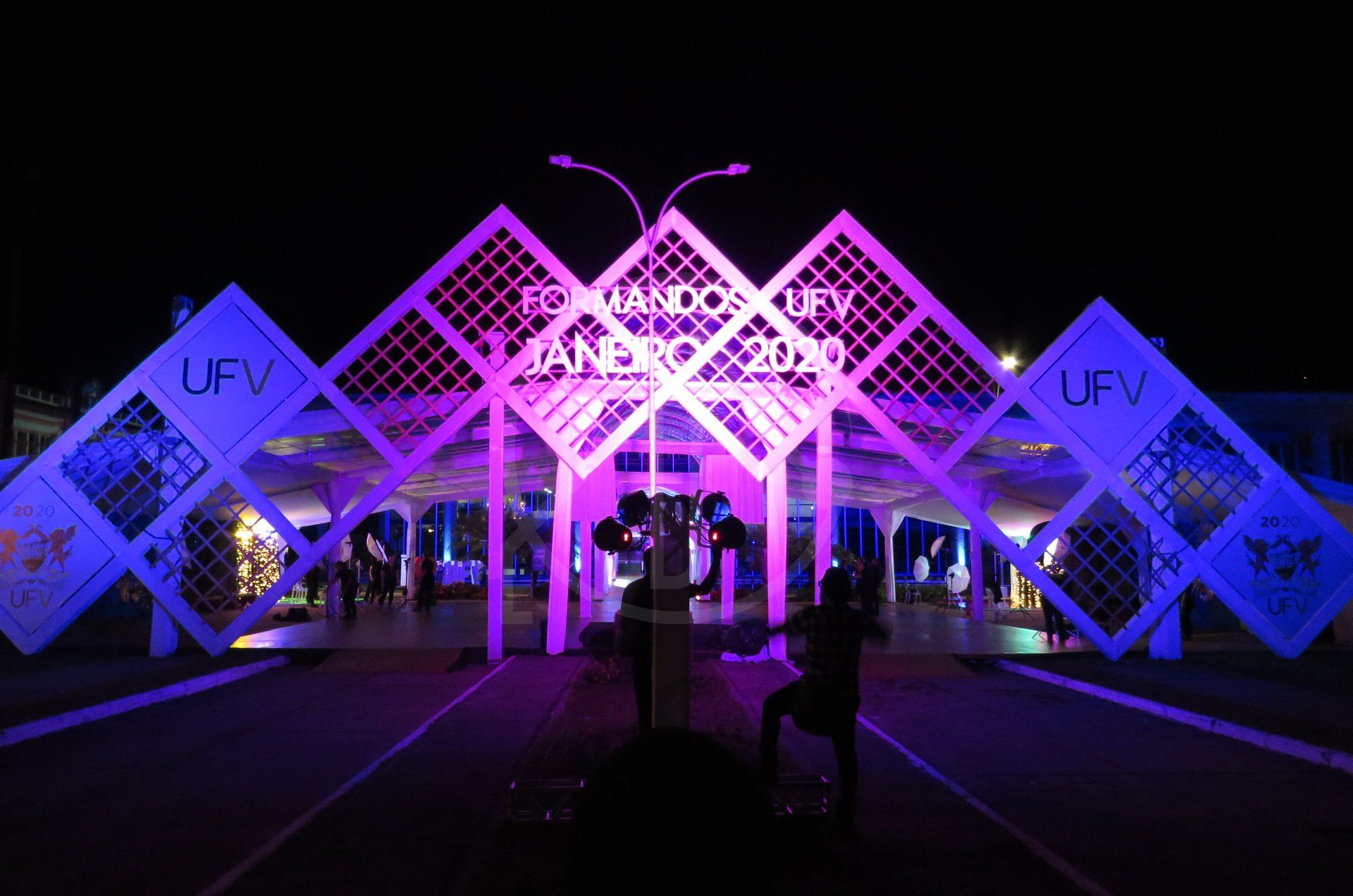 Pórtico em losangos iluminado em roxo durante evento noturno