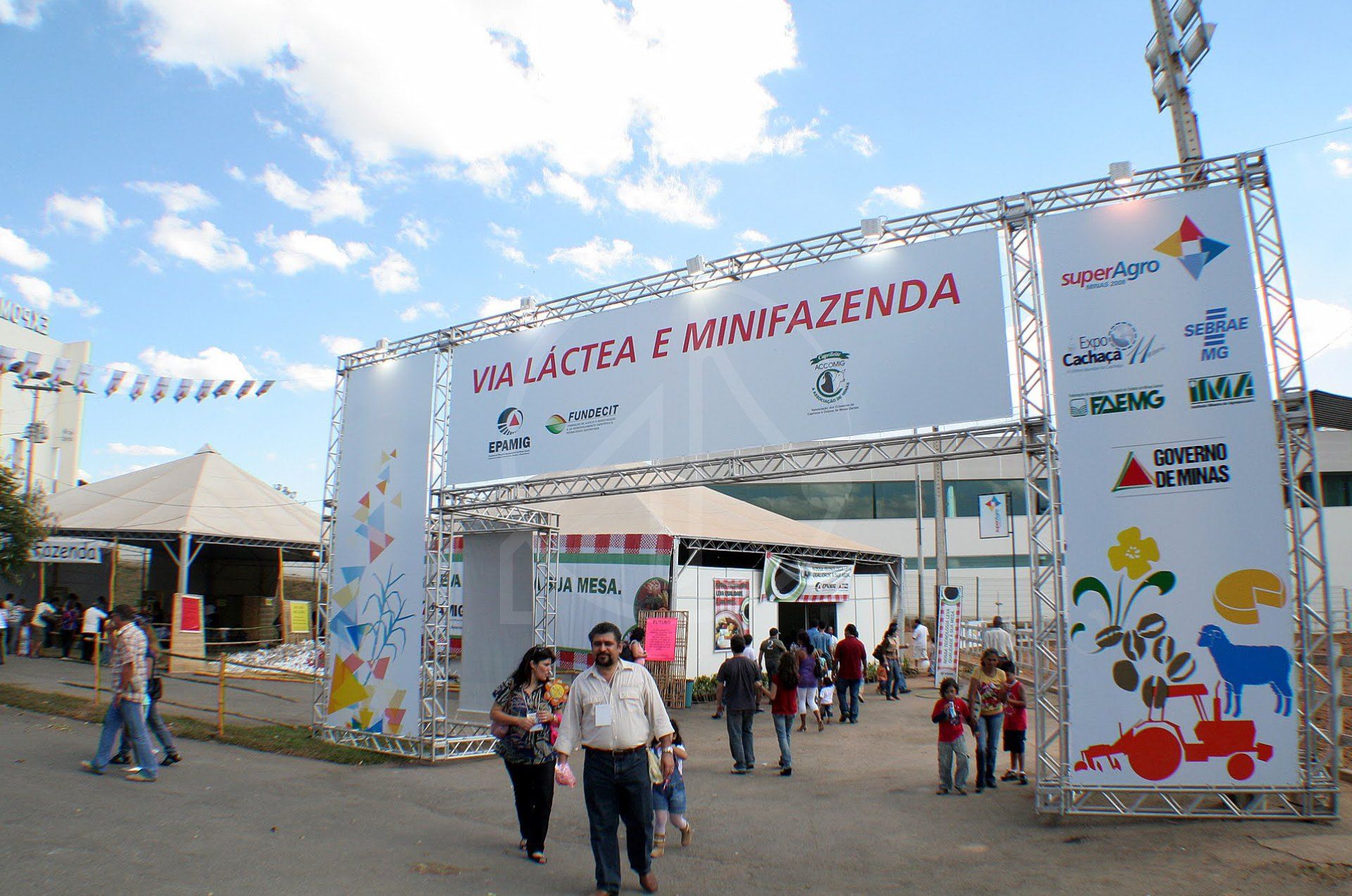 Pórtico de entrada em box truss com a palavra Minifazenda e visitantes passando